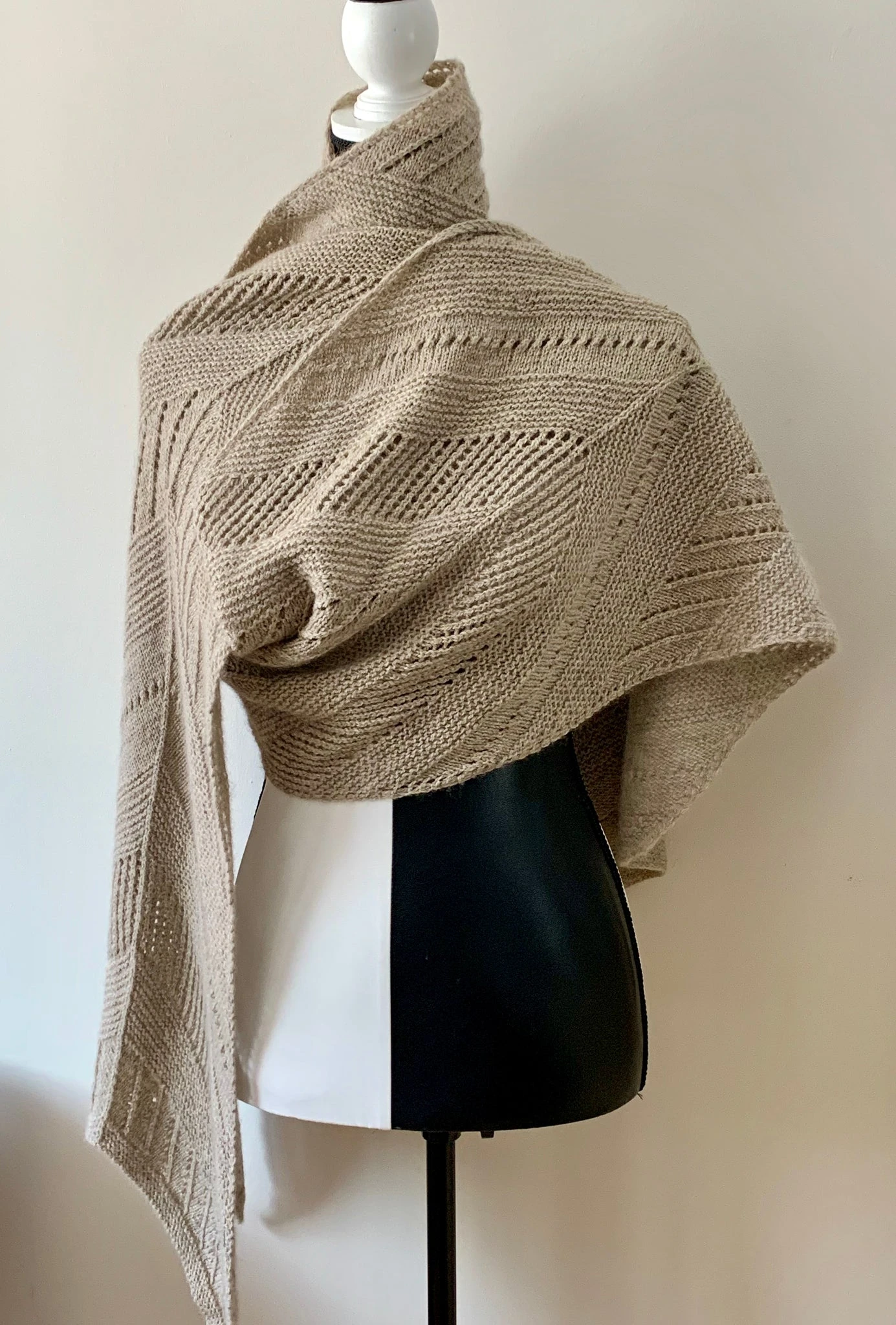 photo of moving forward shawl/wrap knit in beige heavenly blend yarn draped over a black and white mannequin 
